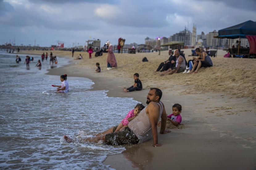 Seorang gadis bersandar pada ayahnya saat mereka menghabiskan waktu di sebuah pantai di Kota Gaza, Minggu, 28 Agustus 2022.