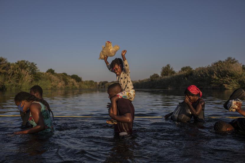 Seorang gadis kecil mengangkat boneka binatangnya tinggi-tinggi di atas air ketika para migran, banyak dari Haiti, menyeberangi sungai Rio Grande dari Del Rio, Texas, untuk kembali ke Ciudad Acuña, Meksiko, Senin, 20 September 2021