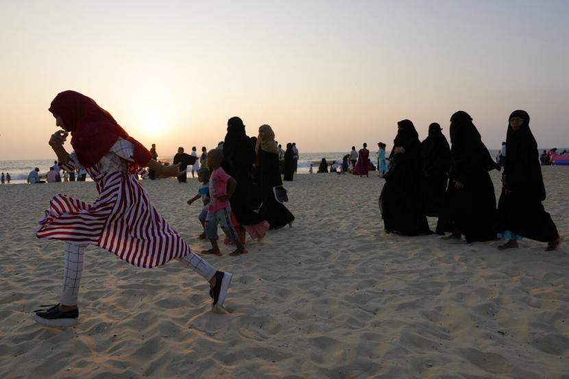 Seorang gadis Muslim India yang mengenakan jilbab berjalan melewati orang lain yang mengenakan burqa pada suatu sore di sebuah pantai di Udupi, negara bagian Karnataka, India, 25 Februari 2022.