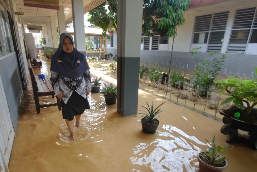 Seorang guru berjalan melewati genangan banjir yang masih merendam sekolah di Batipuhpanjang, Padang, Sumatera Barat, Rabu (23/3).