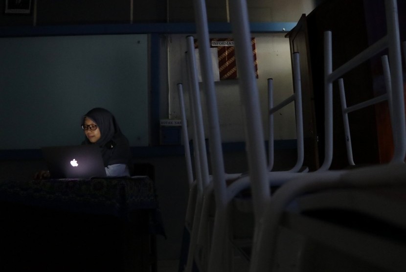 Seorang guru tengah memeriksa tugas muridnya di dalam ruang kelas yang gelap akibat padamnya aliran listrik di MTs Annajah, Jalan Ciledug Raya, Jakarta, Senin (5/8/2019). 
