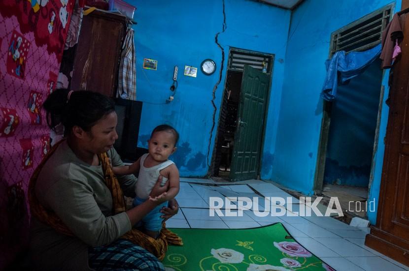 Seorang ibu bermain dengan anaknya di dalam rumahnya yang rusak akibat pergerakan tanah (ilustrasi).