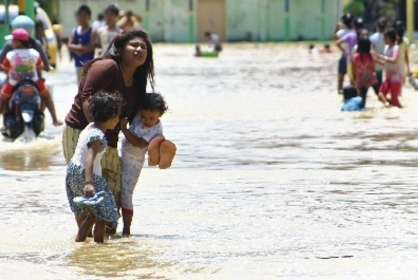 Seorang ibu bersama dua anaknya melewati genangan banjir, di Kabupaten Sampang, Jatim, Sabtu (07/4).