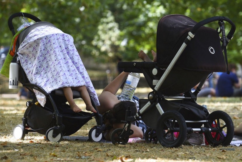 Seorang ibu dan anaknya berteduh di Taman St James di London pada Senin (23/7).