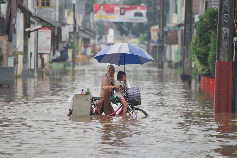  Seorang ibu membawa anaknya mendorong sepeda mereka melintasi banjir yang merendam perumahan Jatikramat Indah di Bekasi, Jawa Barat, Jumat (28/3).  (Republika/Edwin Dwi Putranto)