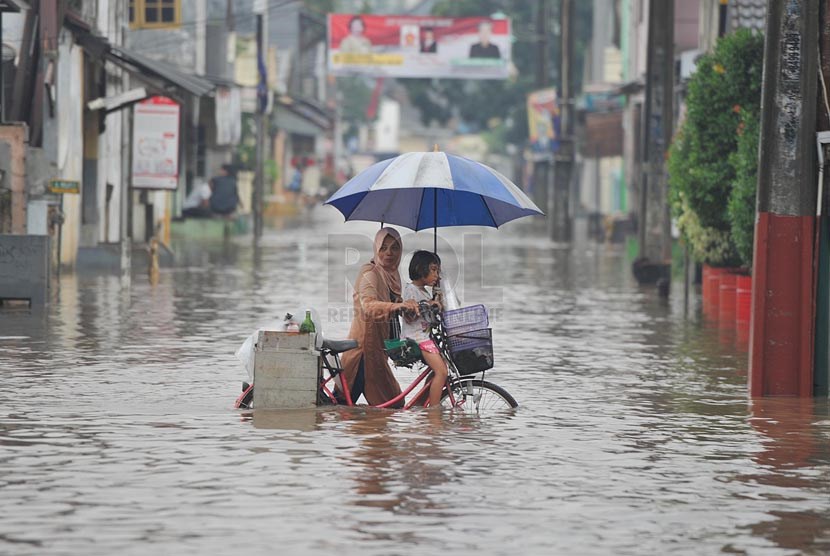 Seorang Ibu membawa anaknya mendorong sepeda mereka melintasi banjir yang merendam perumahan Jatikramat Indah di Bekasi, Jawa Barat, Jumat (28/3).