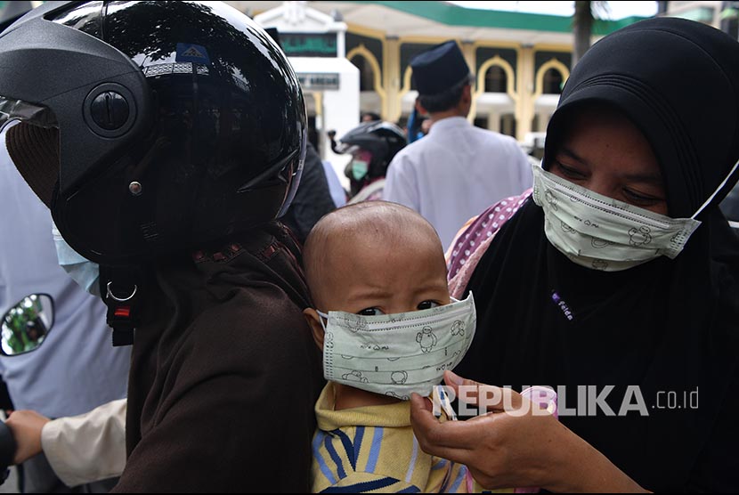 Seorang ibu mengenakan masker pada anaknya 