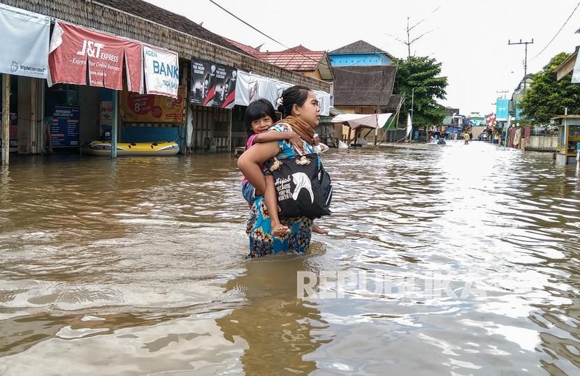 Seorang ibu menggendong anaknya melintasi banjir di permukiman Desa Mentaya Hulu, Kotawaringin Timur, Kalimantan Tengah, di bulan Oktober 2021. Pada November 2021, enam kecamatan di Kotawaringin Timur kembali kebanjiran.