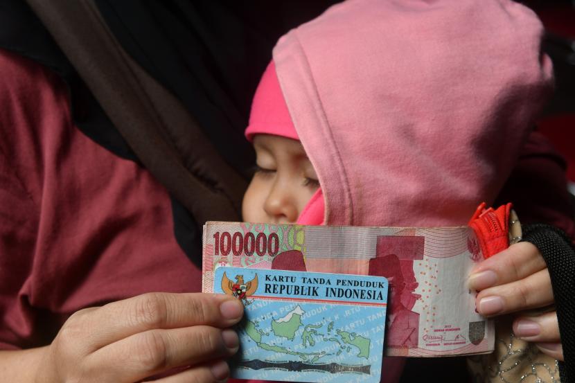 Seorang ibu menggendong anaknya saat penyaluran Bantuan Langsung Tunai (BLT) BBM ilustrasi. Pemerintah Kota Bogor, Jawa Barat segera menyalurkan bantuan langsung tunai (BLT) kepada 2.341 sopir angkutan kota (angkot) dan ojek online pada Oktober 2022 atas dampak penyesuaian harga bahan bakar minyak (BBM).