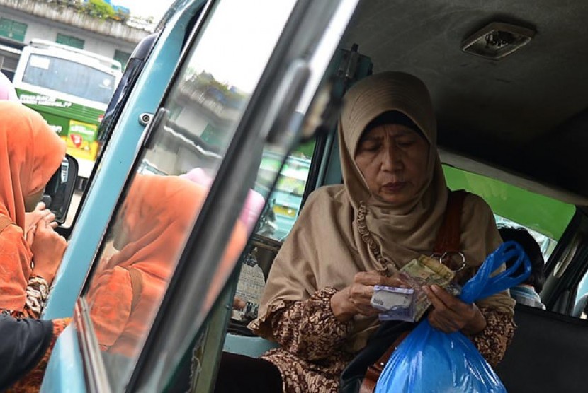 Seorang ibu sedang menghitung uang untuk membayar ongkos angkutan umum. 