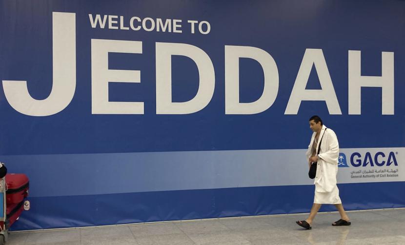 Jamaah Umroh Diizinkan Gunakan Bandara Manapun di Arab Saudi. Foto: Seorang jamaah haji berjalan di depan spanduk penyambutan setibanya di Bandara Internasional King Abdulaziz di Jeddah, Arab Saudi, Jumat, 1 Juli 2022.