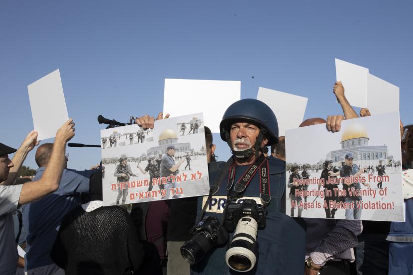 Seorang jurnalis memegang plakat yang menggambarkan polisi sedang memukuli wartawan foto AFP demonstrasi Ahmad Gharabli menentang serangan polisi Israel terhadap jurnalis Palestina, di lingkungan Sheikh Jarrah di Yerusalem timur, Jumat, 28 Mei 2021. 
