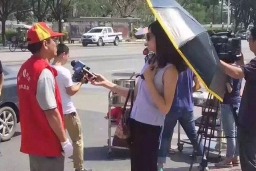 Seorang jurnalis televisi di Cina yang difoto mengenakan kacamata hitam dan payung untuk melindungi diri dari matahari saat mewawancarai sumber dipecat. 