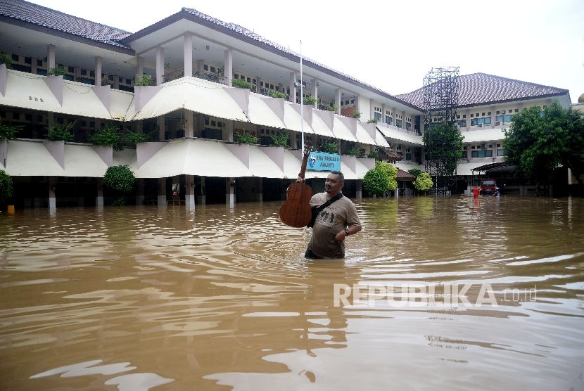  Seorang karyawan melintasi banjir yang menggenagi halaman sekolah SMA Negeri 8 , Bukit Duri, Jakarta (foto ilustrasi).