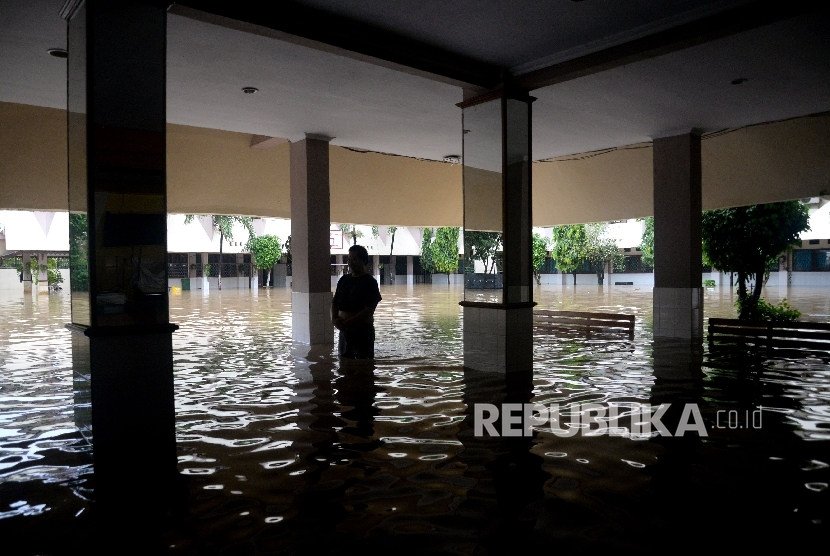  Seorang karyawan melintasi banjir yang menggenagi halaman sekolah SMA Negeri 8 , Bukit Duri, Jakarta, Kamis (16/2).