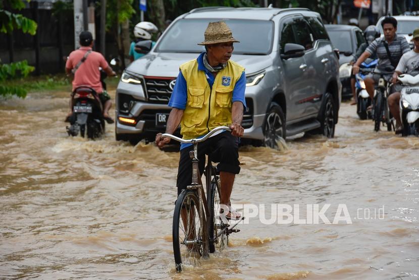 Seorang laki-laki menggunakan sepeda melintasi jalur wisata Mataram - Senggigi yang terendam banjir di Desa Meninting, Kecamatan Batulayar, Lombok Barat, NTB, Selasa (7/12)