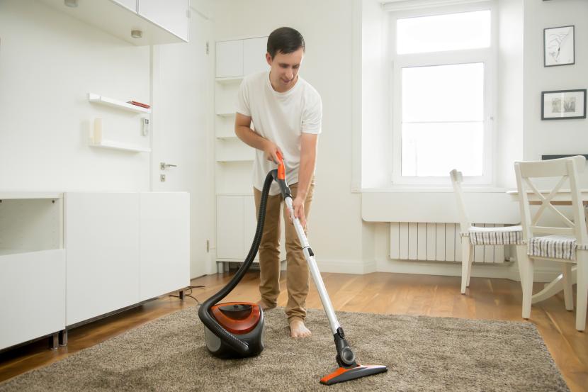 Seorang laki-laki menyedot debu karpet. Ini yang bisa dilakukan ayah di rumah setelah ibu melahirkan.