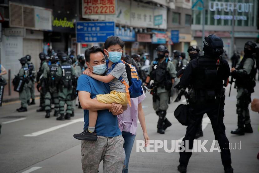  Seorang lelaki menggendong putranya di seberang jalan sementara polisi anti huru hara mendorong kembali para pengunjuk rasa pada hari peringatan penyerahan Hong Kong ke Cina dari Inggris di Hong Kong, Rabu, Juli. 1, 2020. Hong Kong menandai peringatan 23 tahun penyerahannya ke Cina pada tahun 1997, dan hanya satu hari setelah Cina memberlakukan undang-undang keamanan nasional yang menindak protes di wilayah tersebut. 