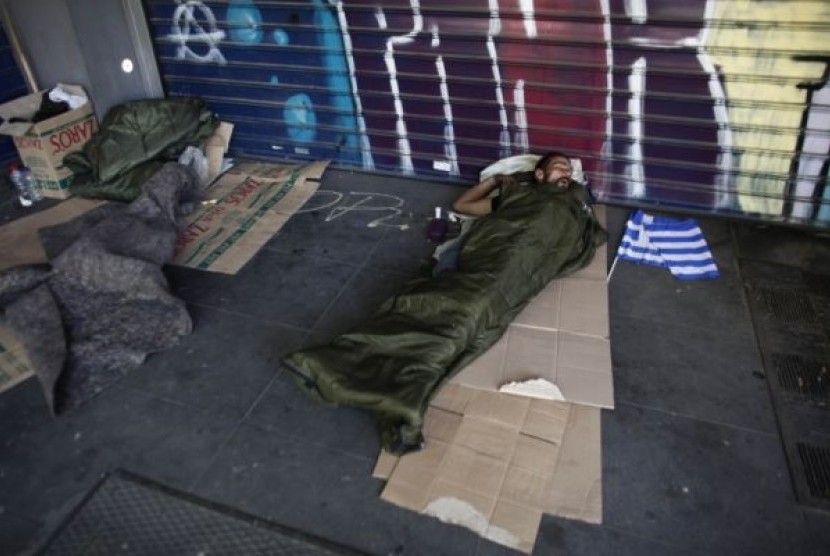 Seorang lelaki tunawisma tertidur di tepi jalan, di samping bendera kecil Yunani yang didapatnya usai menghadiri kampanye pemilu, Sabtu (5/5).
