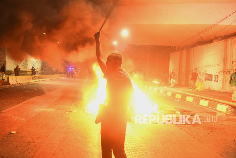 Seorang mahasiswa berdiri dekat api saat bentrok dengan petugas kepolisian saat berunjuk rasa di depan gedung DPR RI, Jakarta, Selasa (24/09/2019). 