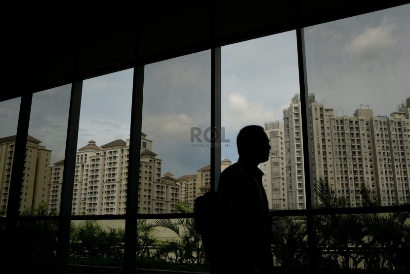 Seorang melintas dari balik kaca dengan latar belakang apartemen di Jakarta, Senin (8/12).