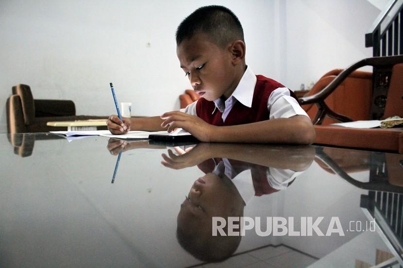 Seorang murid sekolah dasar mengerjakan soal Ujian Akhir Semester (UAS) Genap di rumahnya. Ilustrasi