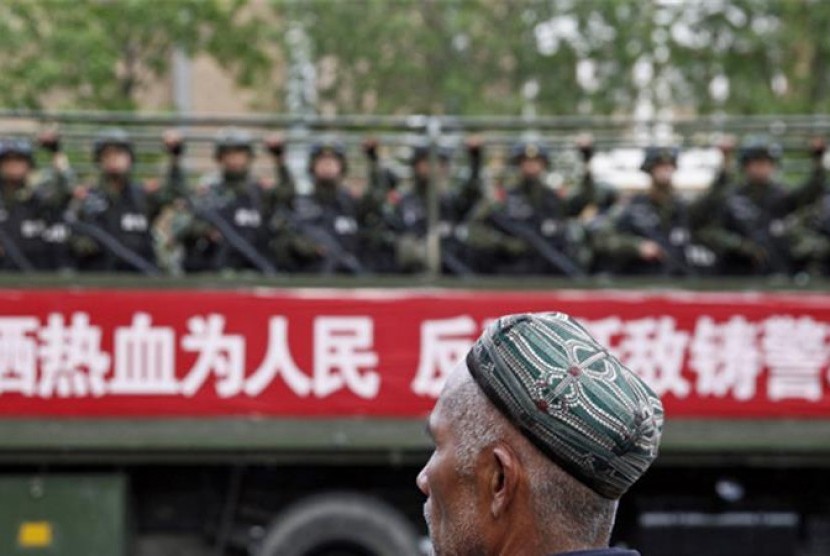 Seorang Muslim Uighur berada di depan militer yang patroli di wilayah Xinjiang.