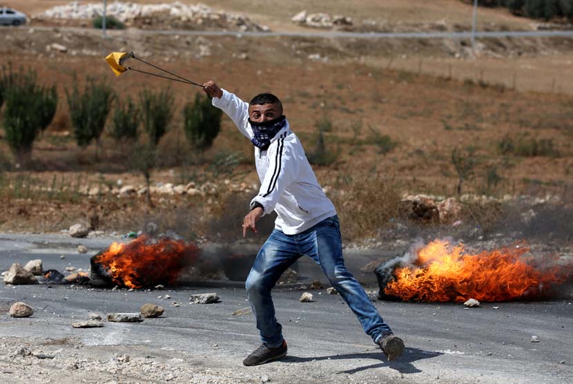 Seorang Palestina melepaskan lemparan batu dalam bentrokan yang pecah di Tepi Barat, Hebron, Palestina, Kamis (8/10). 