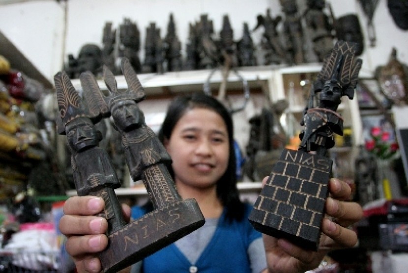 Seorang pedagang menunjukkan patung tari perang dan pakaian adat Nias, di toko cenderamata, Gunung Sitoli, Nias, Sumut, Jumat (18/11). 