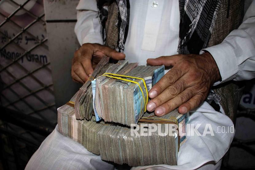 Seorang pedagang penukaran mata uang menghitung Afgani ketika orang-orang berkumpul untuk menarik uang dari sebuah bank di Kabul, Afghanistan, Ahad (12/9).