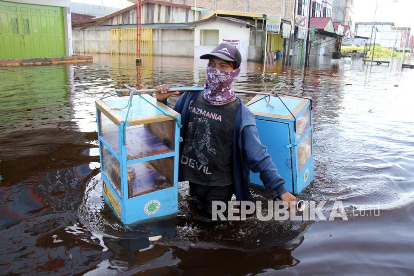 Seorang pedagang roti melintasi genangan banjir di Riau beberapa waktu lalu.