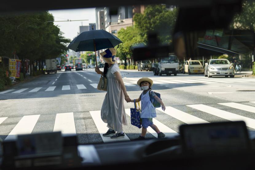 Seorang pejalan kaki menyeberang jalan dengan seorang anak terlihat melalui jendela taksi di Tokyo.