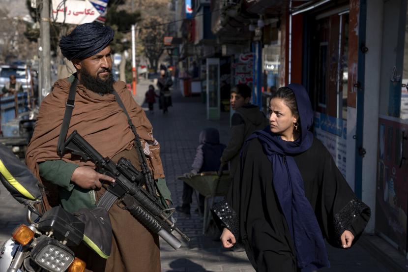  Seorang pejuang Taliban berjaga-jaga ketika seorang wanita berjalan melewati Kabul, Afghanistan, Senin, 26 Desember 2022. Keputusan Taliban baru-baru ini terhadap wanita Afghanistan termasuk larangan pendidikan universitas dan bekerja untuk LSM, yang memicu protes di kota-kota besar. Keamanan di ibu kota Kabul semakin intensif dalam beberapa hari terakhir, dengan lebih banyak pos pemeriksaan, kendaraan bersenjata, dan pasukan khusus Taliban di jalanan. Pihak berwenang belum memberikan alasan untuk keamanan yang lebih ketat.