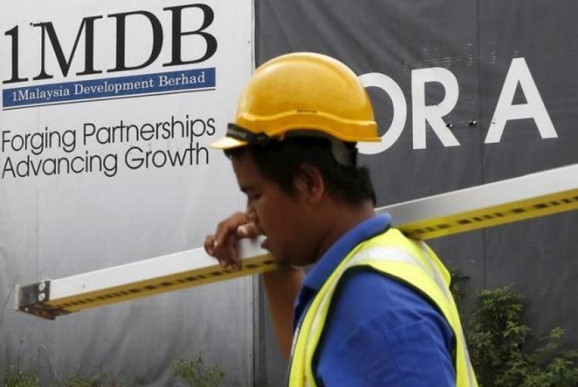 Seorang pekerja konstruksi berjalan melewati plang bertuliskan 1Malaysia Development Berhad (1MDB)