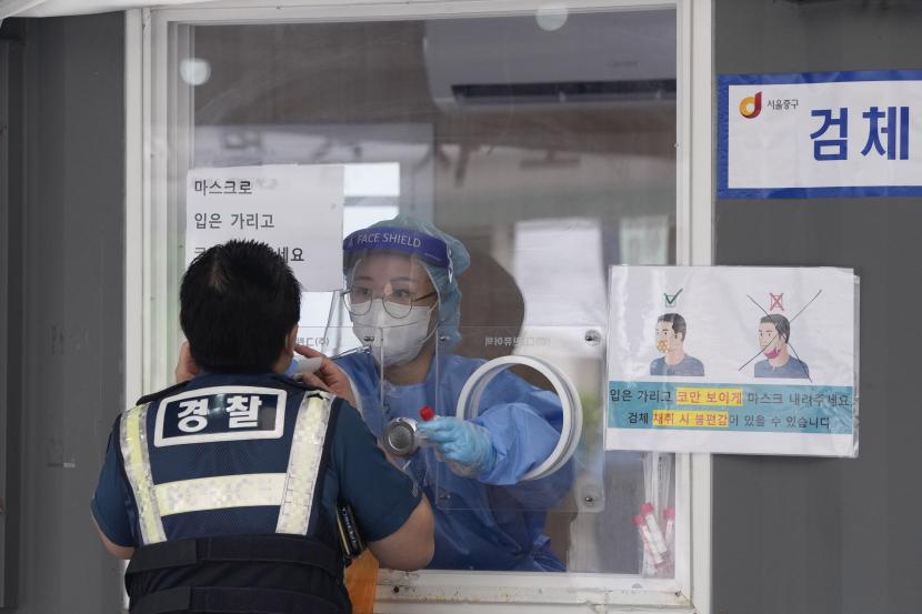 Seorang pekerja medis di sebuah bilik mengambil sampel hidung dari seorang petugas polisi selama pengujian virus corona di tempat pengujian darurat di Seoul, Korea Selatan, Sabtu, 25 September 2021.