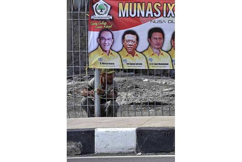   Seorang pekerja memasang bendera dan spanduk Musyawarah Nasional (Munas) IX Partai Golkar di pagar pembatas Tol Bali Mandara saat persiapan kegiatan tersebut di Nusa Dua, Bali, Jumat (28/11).  (Antara/Nyoman Budhiana)