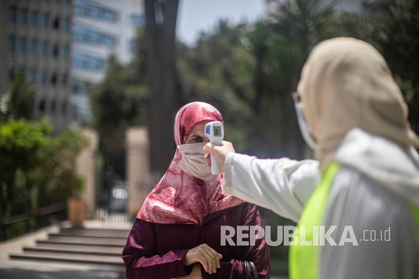 Seorang pekerja memeriksa suhu orang yang akan sholat di masjid di Rabat, Maroko. Raja Maroko sudah mengumumkan, warga akan memperoleh vaksin Covid-19 secara gratis.