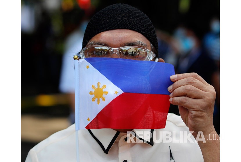 Seorang pekerja pemerintah Filipina menunjukkan sebuah bendera Filipina. Sekitar 1.400 warga Filipina menggelar unjuk rasa untuk memperingati revolusi 1986, Sabtu (25/2/2023).