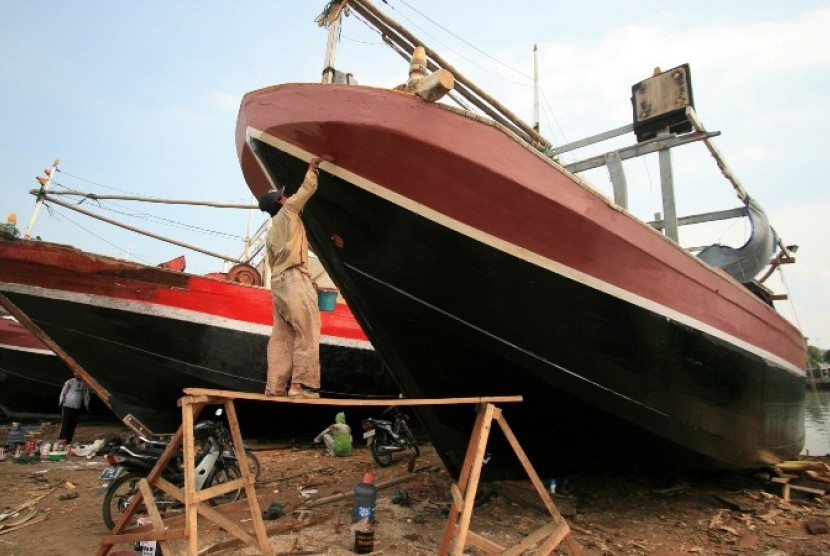 Seorang pekerja sedang memperbaiki kapal yang rusak. Bantuan pemerintah berupa kapal fiber banyak dikeluhkan nelayan karena bingung mengoperasikan
