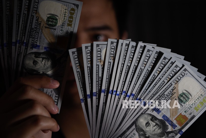 Seorang pembeli menunjukkan uang Dolar Amerika Serikat yang ditukarnya di gerai penukaran valuta asing, Jakarta, Senin (15/7/2019).