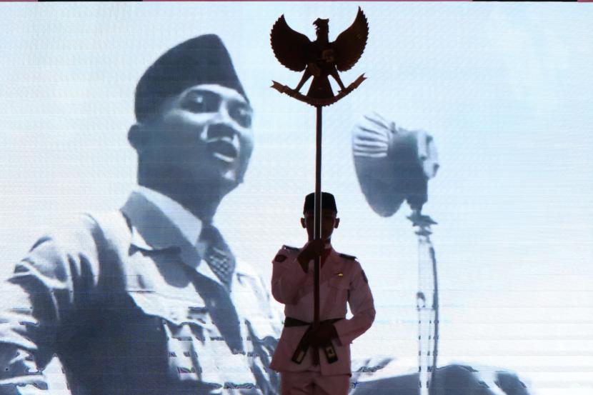 Seorang pemuda membawa Garuda Pancasila di depan layar yang menampilkan Proklamator Soekarno.