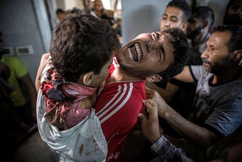 Seorang pemuda Palestina berduka memegang mayat adiknya, salah satu dari empat anak laki-laki yang tewas dalam serangan Israel di Gaza.