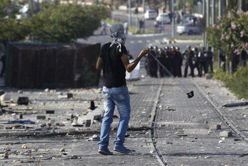 Seorang pemuda Palestina melakukan perlawanan dengan menggunakan batu menghadapi barisan tentara Israel. (ilustrasi) 