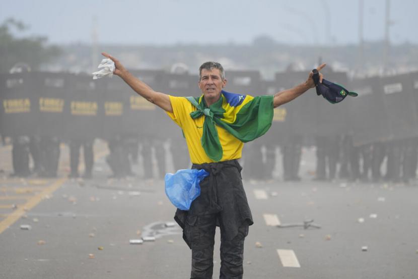 Seorang pendukung mantan presiden Jair Bolsonaro berdiri di depan barisan polisi huru-hara saat aksi penyerbuan ke istana kepresidenan di Brasil.
