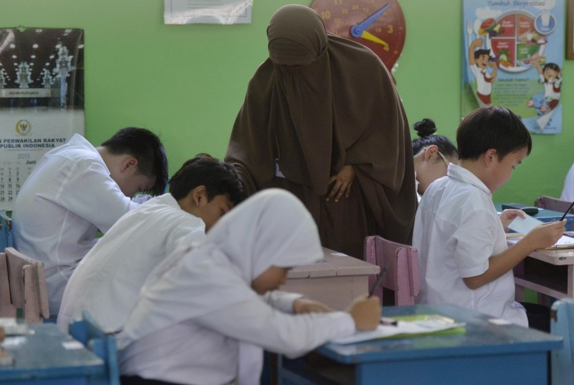 Seorang pengawas membantu peserta mengisi identitas peserta sebelum mengikuti ujian paket A atau setara SD di SDN Gondangdia 1 Pagi, Jakarta, Senin (18/5).