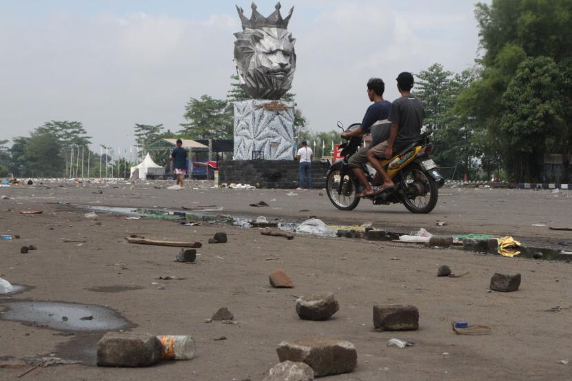 Seorang pengendara motor melintas diantara puing batu yang dilemparkan suporter dalam kerusuhan di Stadion Kanjuruhan, Malang, Jawa Timur, Ahad (2/10/2022). Polda Jatim mencatat data sementara korban jiwa dalam kejadian tersebut berjumlah 127 orang dan 13 kendaraan rusak. 