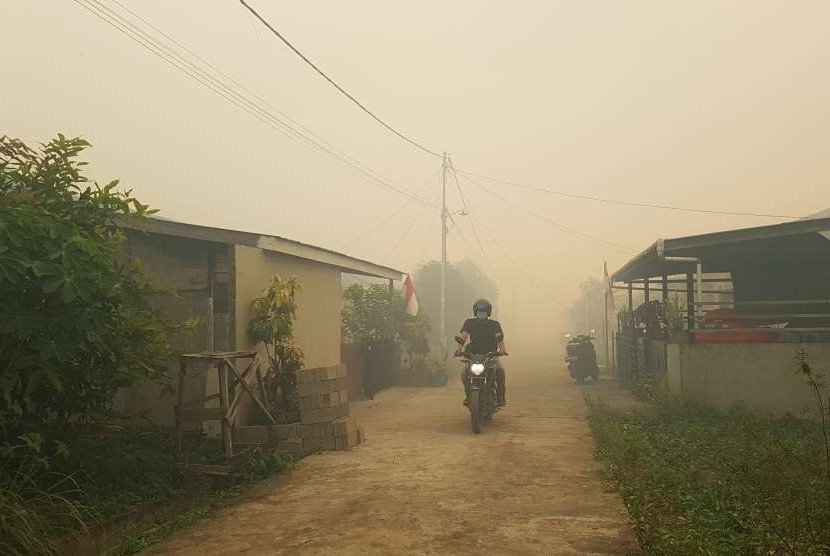 Seorang pengendara motor melintasi perumahan yang tertutupi kabut asap (ilustrasi)