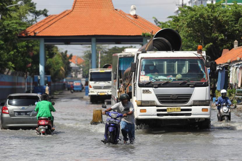 Seorang pengendara motor mendorong kendaraannya melintasi banjir rob di Jalan Kalimas Baru, Surabaya, Jawa Timur.