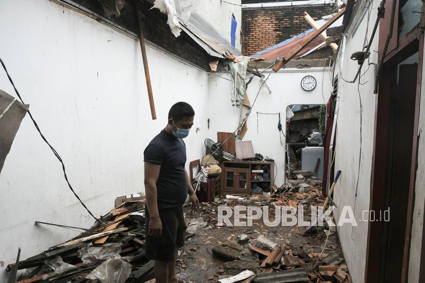 Seorang penghuni rumah mengamati bagian rumah yang rusak akibat angin kencang (ilustrasi).