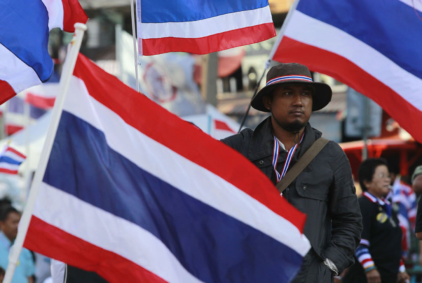  Seorang pengunjuk rasa anti-pemerintah berdiri di samping bendera nasional Thailand, saat berunjuk rasa di pusat kota Bangkok (15/1).   (Reuters/Chaiwat Subprasom)
